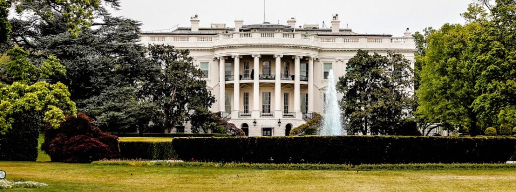 A photo of the White House from the front, with trees on either side framing the picture.